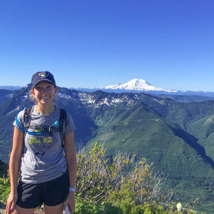 Molly Polizotto on mountain top with snow covered mountain in the distance